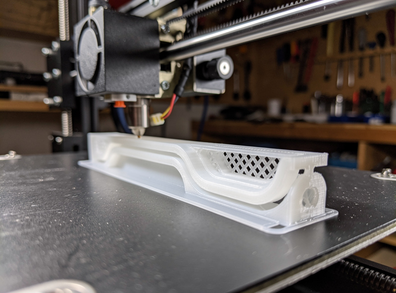3D printer mid-print depositing a white PETG edge slicker with visible perimeter walls and parametric groove geometry on the build plate, soft workshop light, photographic realism