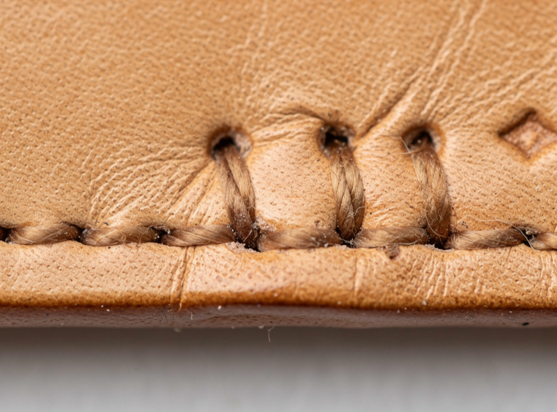 Close-up of beginner saddle stitching showing uneven stitch length and divergent thread on tan veg-tanned leather
