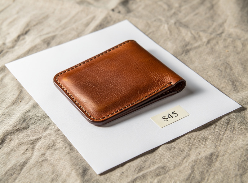 Etsy-style product photograph of a hand-stitched leather wallet with a price tag on white paper, neutral linen background