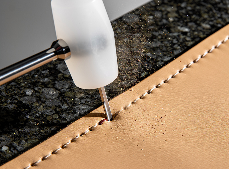 Diamond stitching chisel struck with a poly mallet on granite stone, marking 4 mm spaced stitch holes on tan veg-tanned leather