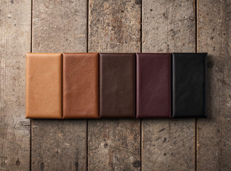 Five small leather samples dyed in different shades from natural to walnut to dark brown to mahogany to jet black on a wooden board