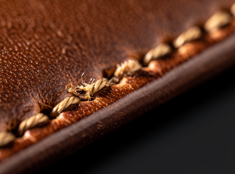 Close-up of a brown leather wallet seam hand-stitched with contrasting tan waxed thread showing even slanted stitches