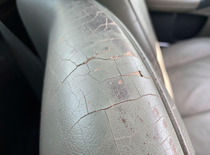 Close-up of a cracked and faded car leather seat bolster showing surface cracking and worn color