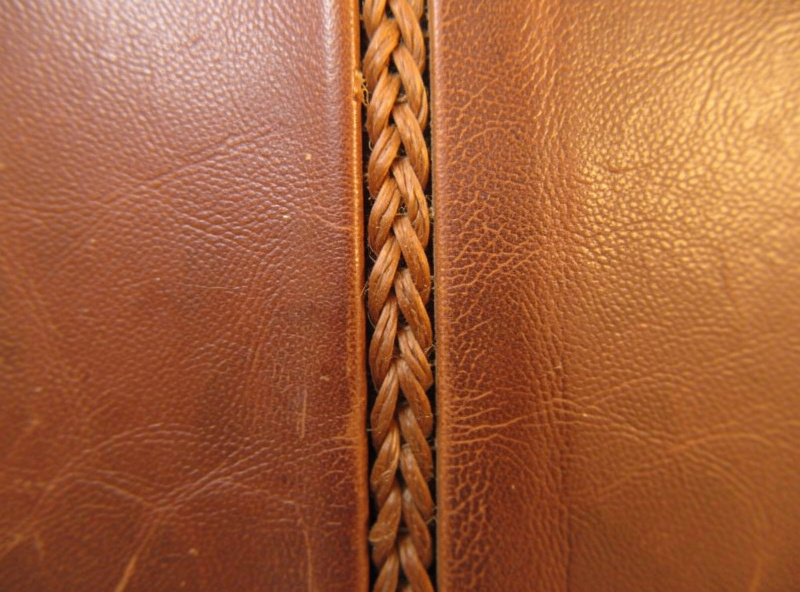 Close-up of an exposed Coptic chain stitch running down a book spine between leather covers