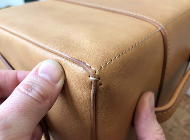 Saddle-stitched exposed gusset seam being burnished on the boxed corner of a leather dopp kit