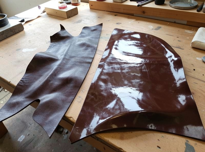 Hardened darkened cuir bouilli leather pieces alongside a wax-finished molded panel on a workbench