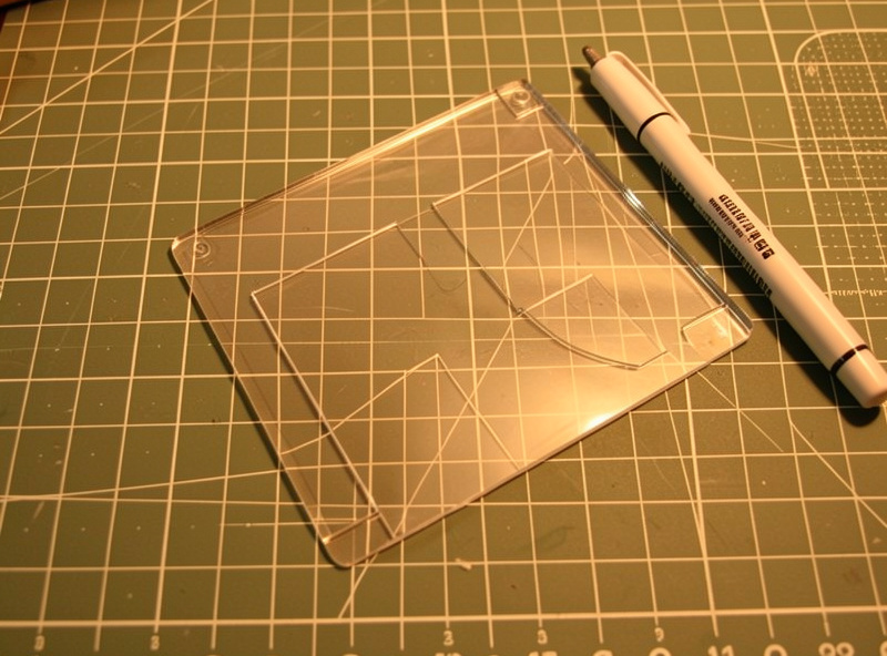 A clear acrylic card-holder pattern template on a cutting mat with a marking pen