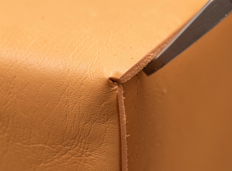 An edge beveler shaving the corner off a thick tan leather edge