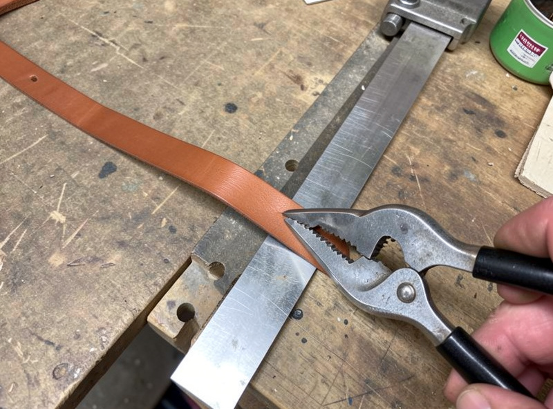 A long leather strap being cut from a bridle leather bend against a steel straightedge