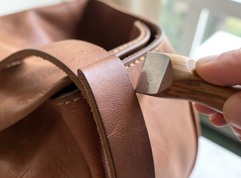 Slicking the beveled edge of a doubled leather bag strap with a profiled edge slicker