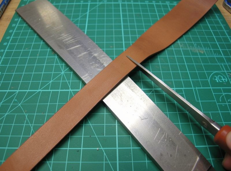 Cutting a one-inch bridle leather strap against a steel straightedge with a rotary cutter on a self-healing mat
