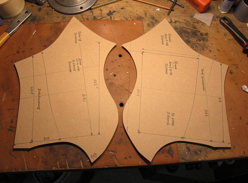 Paper pattern pieces for a leather dog harness laid out on a workshop bench with measurements marked