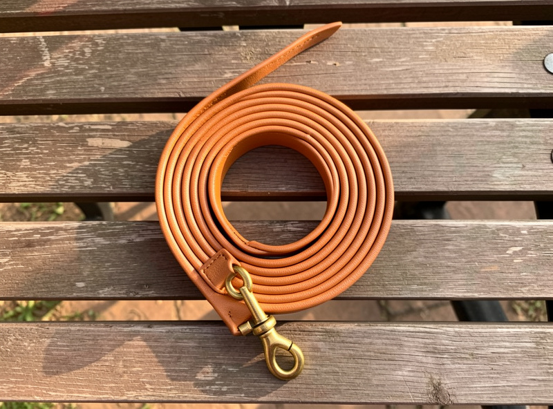 A coiled hand-stitched bridle leather dog leash with a brass swivel snap on a workshop bench