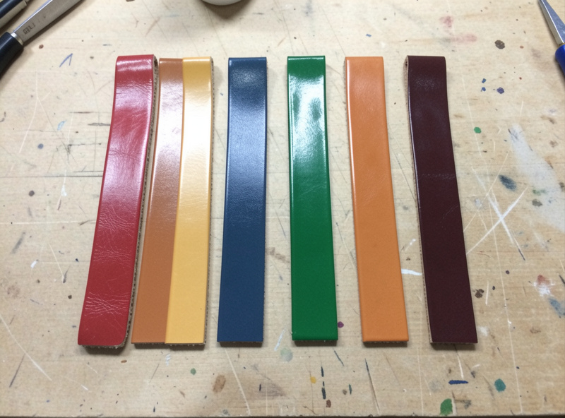 Three bottles of leather edge paint beside test strips of painted leather edges in different colors