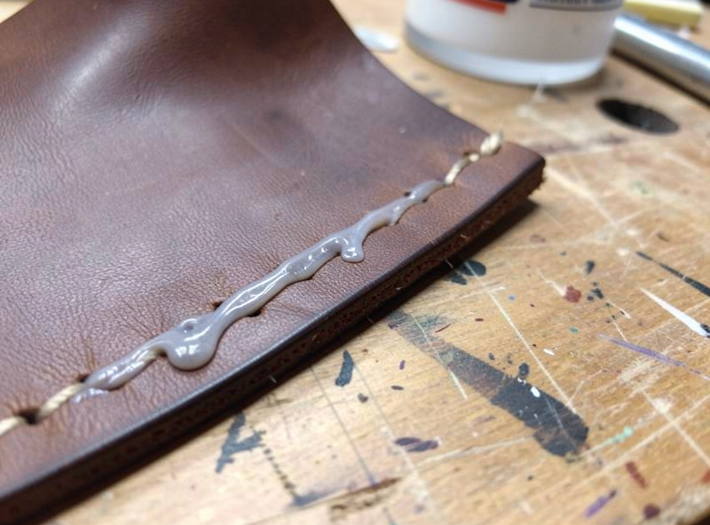 Damp leather sheath being boned tightly around a plastic-wrapped knife on a workbench