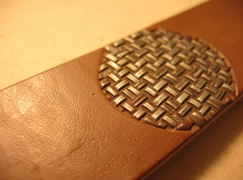 A leather belt blank stamped with an even repeating basketweave pattern beside the basketweave stamp