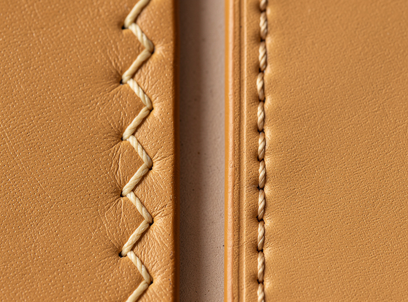 Two leather samples side by side showing a slanted European-style stitch line next to a straighter Asian-style stitch line on tan leather