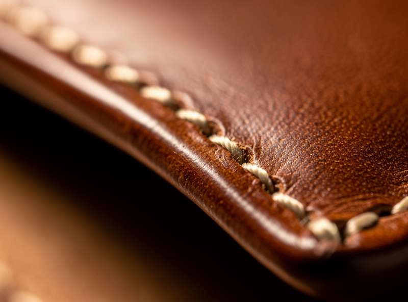 Close-up of a finished brown leather wallet edge showing a clean stitch line running parallel to a beveled and burnished slicked edge