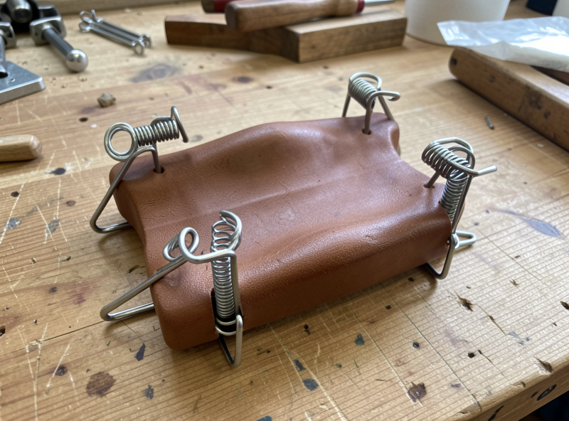 A molded leather piece held with spring clamps drying on a workshop bench