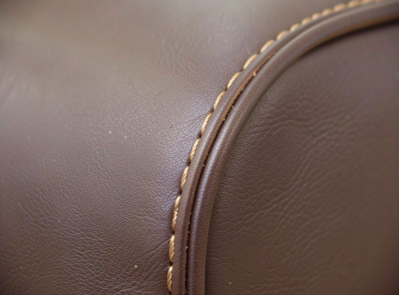 A contrast tan topstitch line in bonded thread along the edge of a dark brown leather bag panel