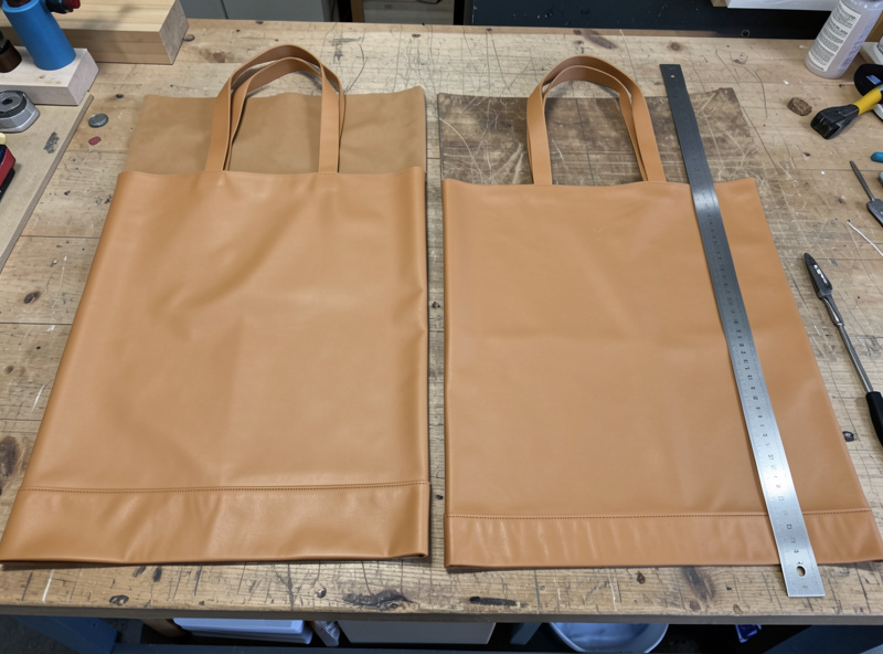 Two large leather tote panels, a base gusset strip, and two handle straps cut and laid out on a workshop bench