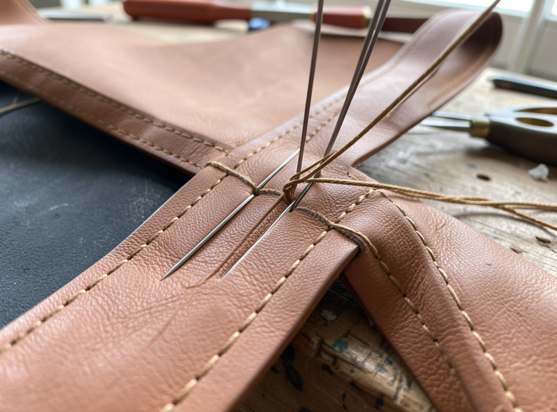 A long leather tote gusset seam being saddle-stitched in a stitching pony with two needles and waxed thread