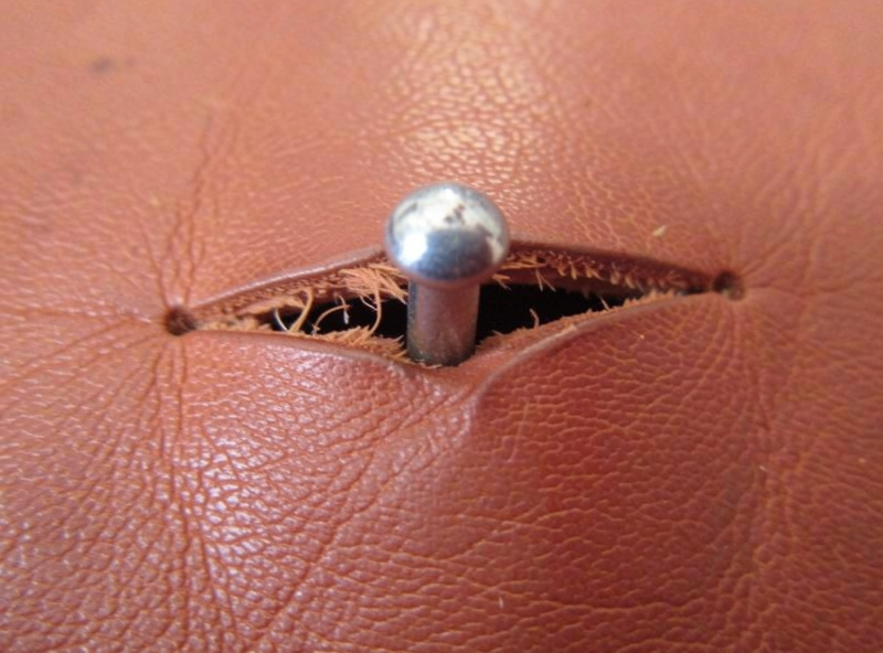 Macro of a rivet that has torn a slot through a single thin leather layer, showing pull-through failure