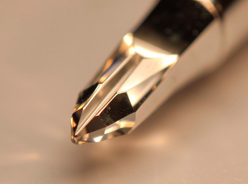 Macro close-up of a polished four-faced diamond awl blade tip catching warm light with a mirror finish
