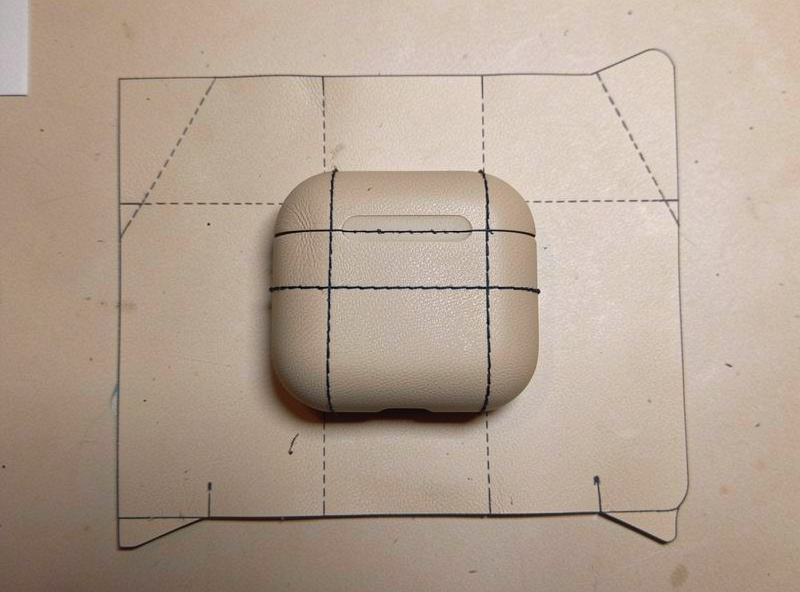 Flat leather AirPods case pattern with fold lines, test-fit around a charging case
