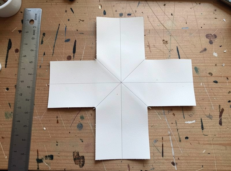 Cross-shaped veg-tan leather blank laid flat with wall fold lines marked in pencil beside a ruler