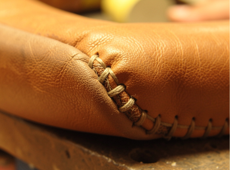 Close-up of a rolled leather rim stuffed with cord filler being stitched down to form a padded edge