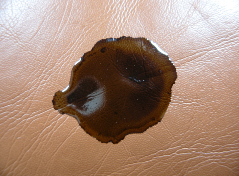 Dark oil stain soaked into tan leather with a translucent shadow around the edge