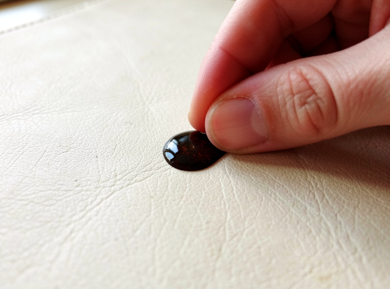 Leather worker placing a drop of water on veg-tan leather to test absorbency before stain removal